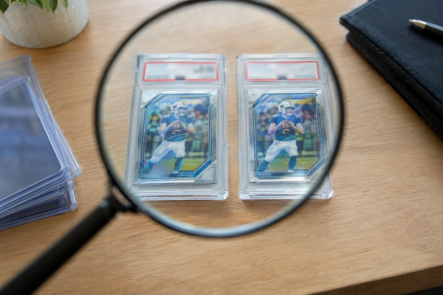 Two PSA-graded trading card slabs side by side on a desk under a magnifying glass for comparison