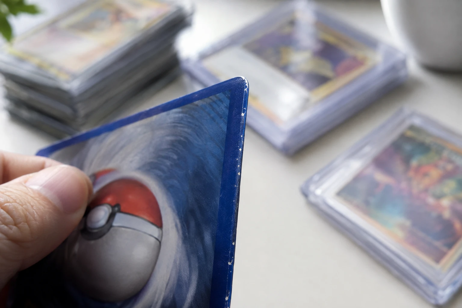 Close-up of a Pokemon card edge held at an angle showing white specks along the blue border